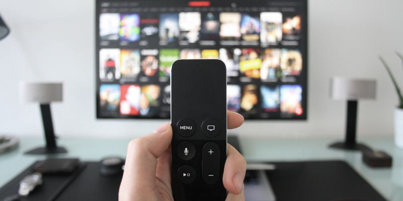 Image of hand holding streaming stick with TV streaming services in the background.