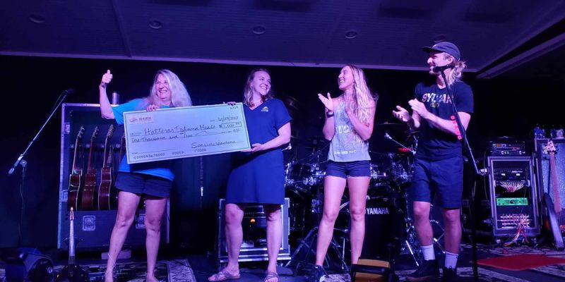 Seaside Vacations’ Lori Smith presents a check to Hatteras Island Meals at Thursday’s Koru Beach Klub concert