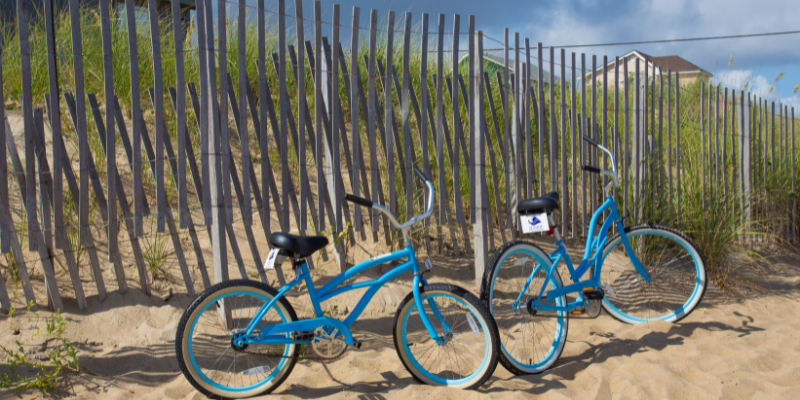 Blue bikes resting against sand dunes at the beach.