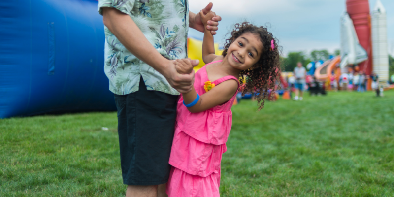 Dad and daughter dancing outside in front of an inflatable slide.