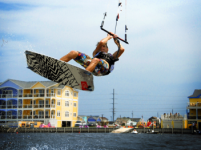 Man in a colorful bathing suit kiteboarding on the sound with a yellow and blue hotel in the background.