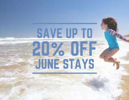 Jump Into June Sale Young girl jumping into the shoreline on a sunny beach.