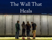 Three people standing in front of a replica of the Vietnam War memorial in DC.