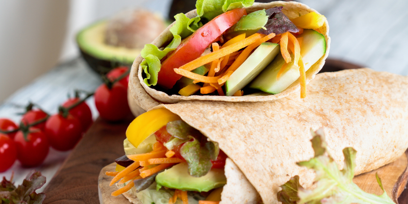Image of whole wheat tortilla filled with cucumbers, carrots, tomatoes, and lettuce.