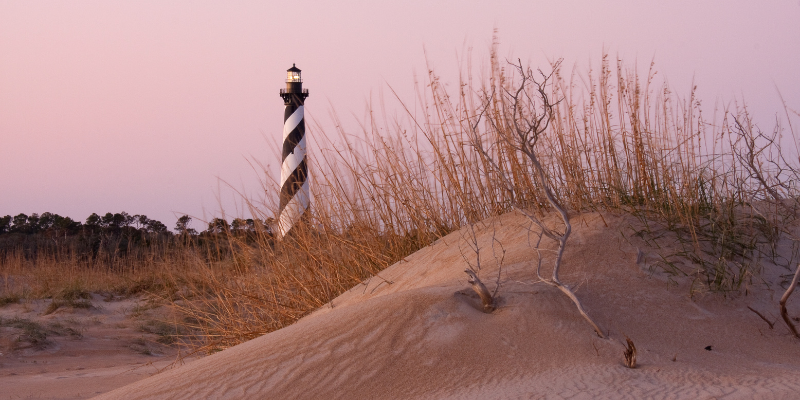 Cape Hatteras Lighthouse in background behind small sand dune.