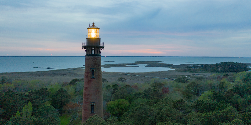 Image of Currituck Beach Lighthouse with light glowing in front of marsh/sound.