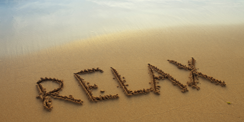 The word "relax" written in the sand on beach.