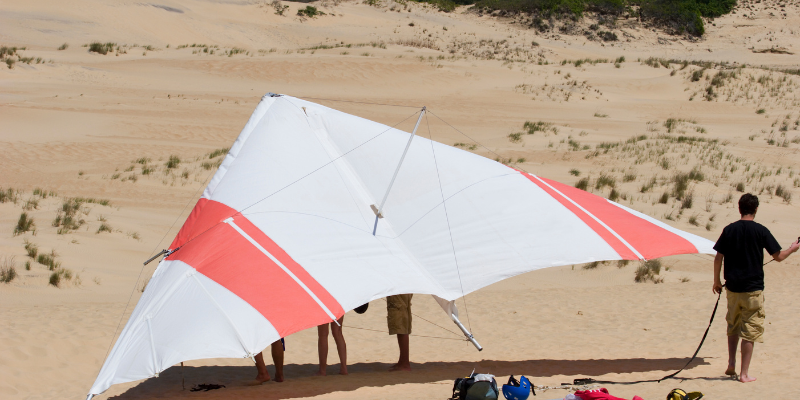 Red and white hang glider resting on the sand.