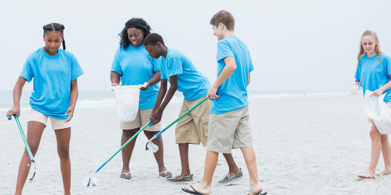 Group of young people wearing blue shirts cleaning up trash on the beach.