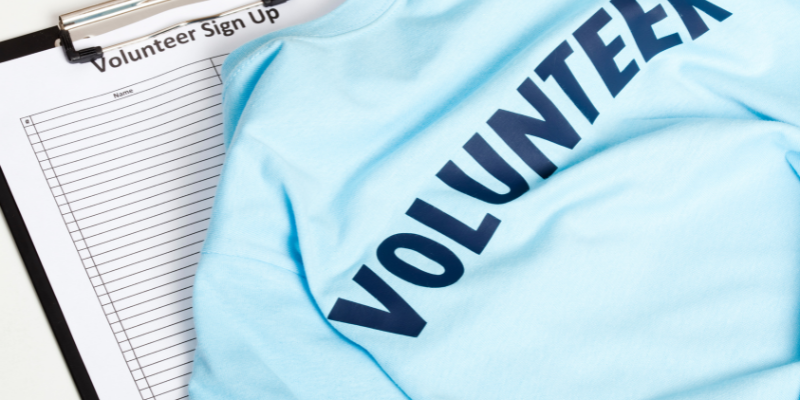 Blue shirt reading "Volunteer" in front of signup sheet.