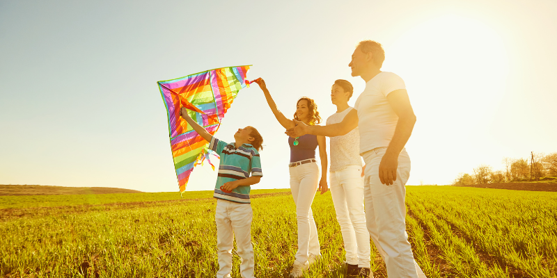 Family playing with a kite in a field at sunset.