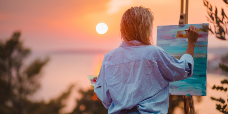 Woman painting a sunset on the water.