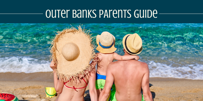 Mom, dad, and son sitting on the shore in front of the ocean.