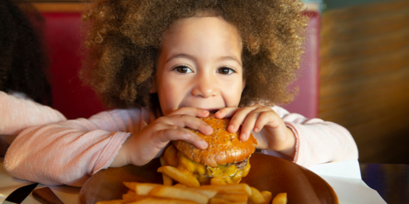 Young girl eating a hamburger at a restaurant.