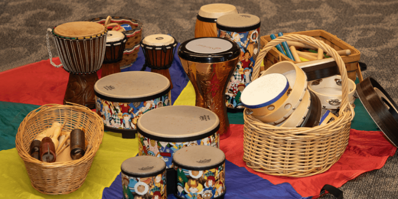 Family Music Time - Duck Town Events Collection of drums in a circle on rainbow tarp.