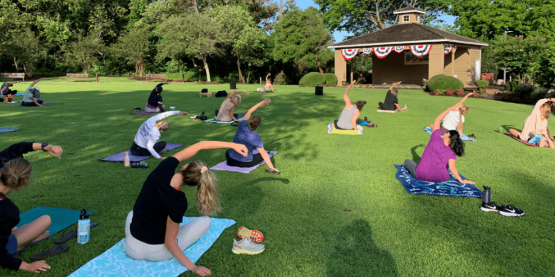 Group of people doing yoga on a green lawn.