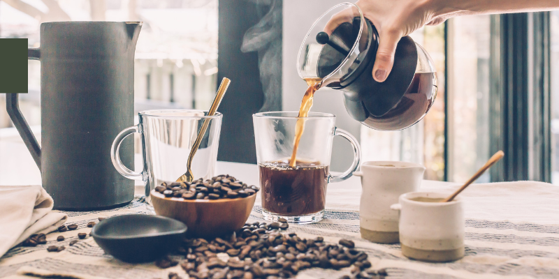 Image of someone pouring coffee into mug; surrounded by coffee beans.