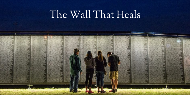 Four people standing in front of a replica of the Vietnam War memorial in DC.