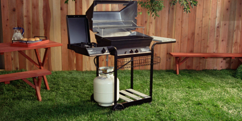 Image of grill on green grass with fence in background.
