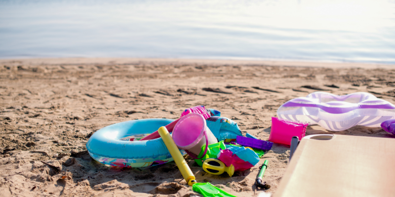 Image shows a sandy beach with pool rings, fins, and other beach gear strown about.