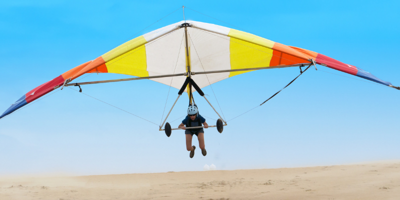 Image of a person hang gliding across sand dunes.