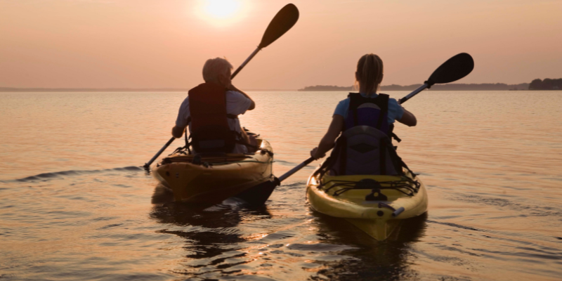 Image of two people kayaking into the sunset.