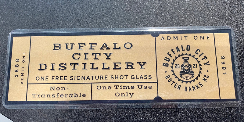 A tan laminated ticket with the words "Buffalo City Distillery One Free Signature Shot Glass."