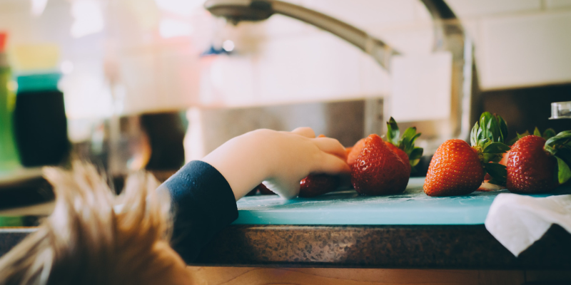 Out of focus image of child reaching onto counter for strawberries.
