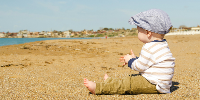 Picture of baby sitting on a beach wearing a newsboy cap.