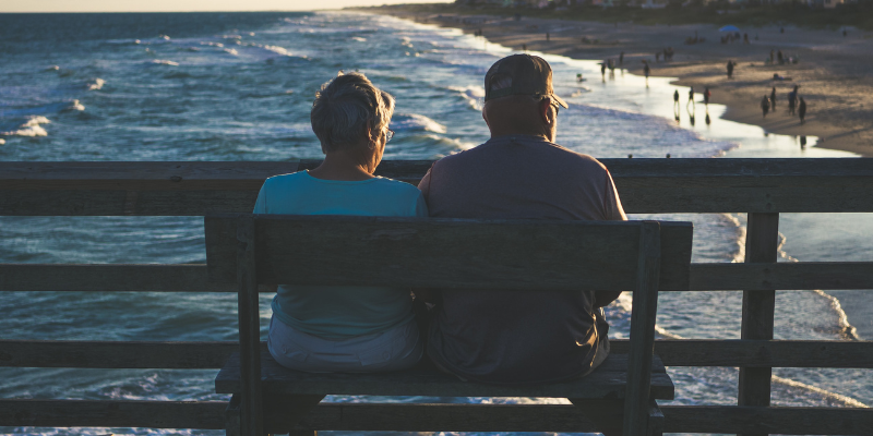 Image of a man and woman sitting together on a pier by the ocean.