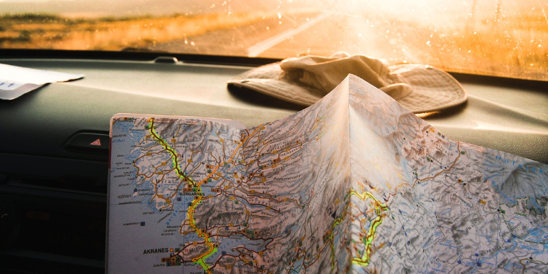Image of map on top of dashboard with road and sunset in background.