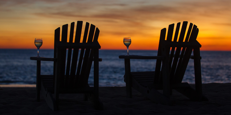 Two beach chairs with wine glasses on the arm rests.