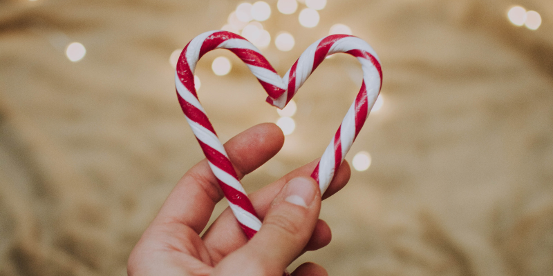 Candy canes shaped like a heart against sandy background with lights.