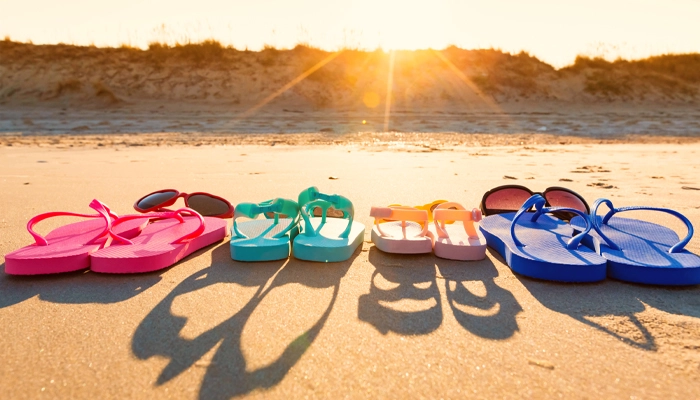 4 pairs of brightly colored flip flops and two pairs of sunglasses sitting on the sand 