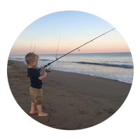 Small child holding a fishing rod looking out at the ocean 