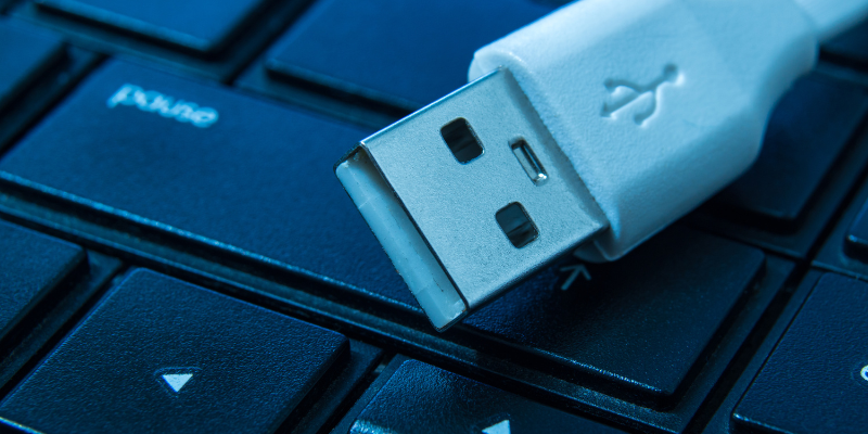 Ending of a charger cord sitting on top of a computer keyboard.